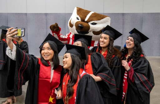 Students in caps and gowns take a selfie with Bucky Badger.