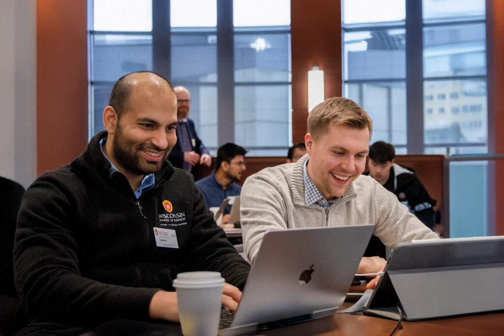 Two male students smile as they work next to each other at a table.