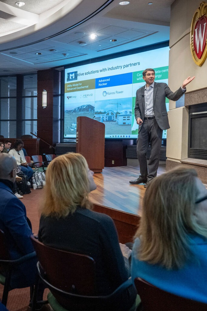A speaker points to a slide while presenting onstage at AI Day.