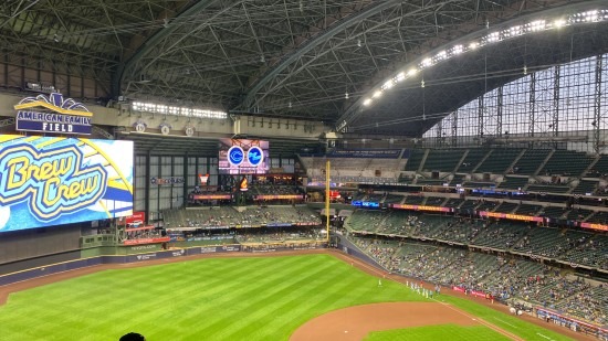 A wide-angle view of the Milwaukee Brewers' stadium, showing the field, seating tiers, jumbotron, and roof.