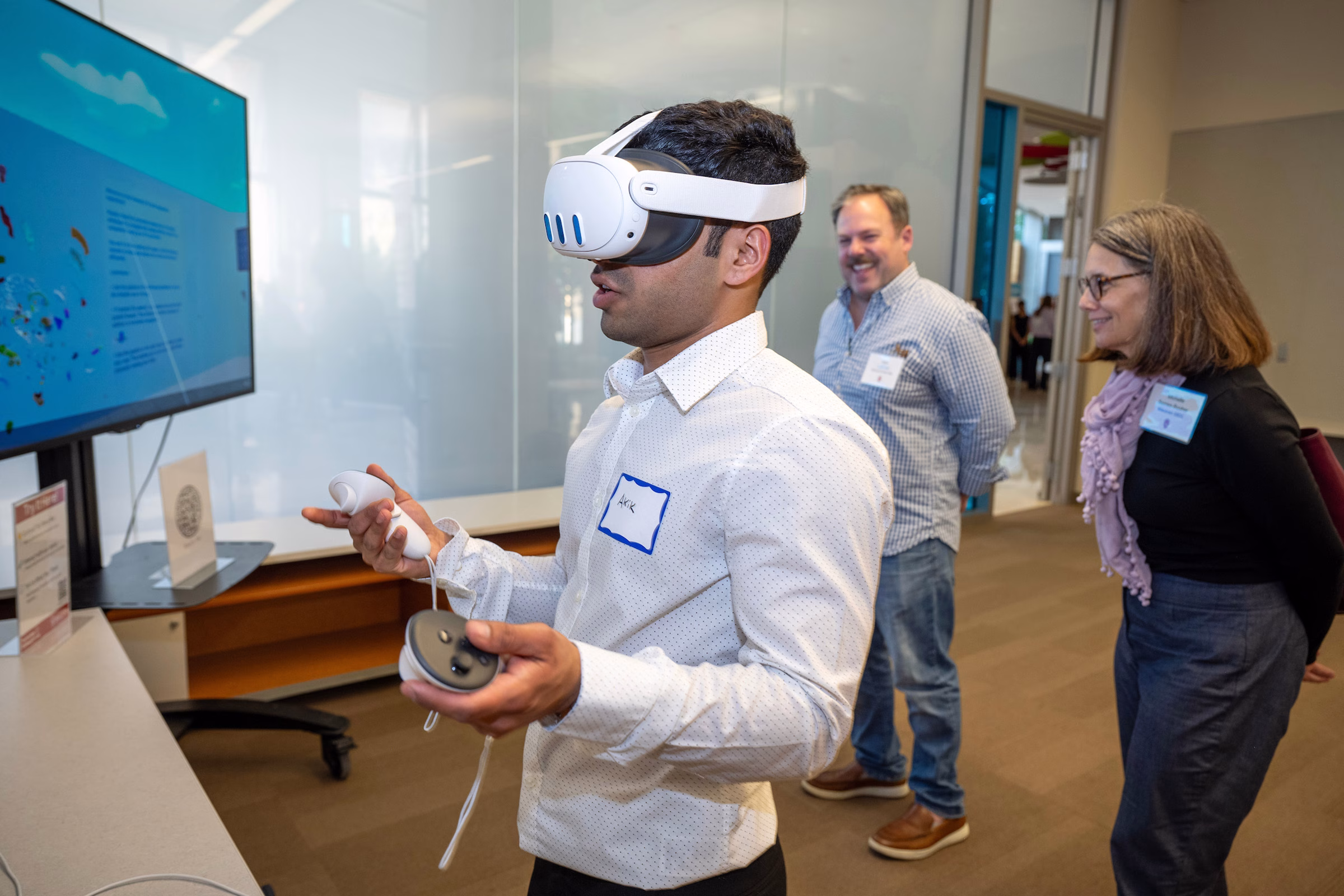 Student Akik Aziz (BS ‘25) showcases his semester-long project at UW–Madison’s Tech Exploration Lab while wearing a VR headset. Two people stand behind him, watching.