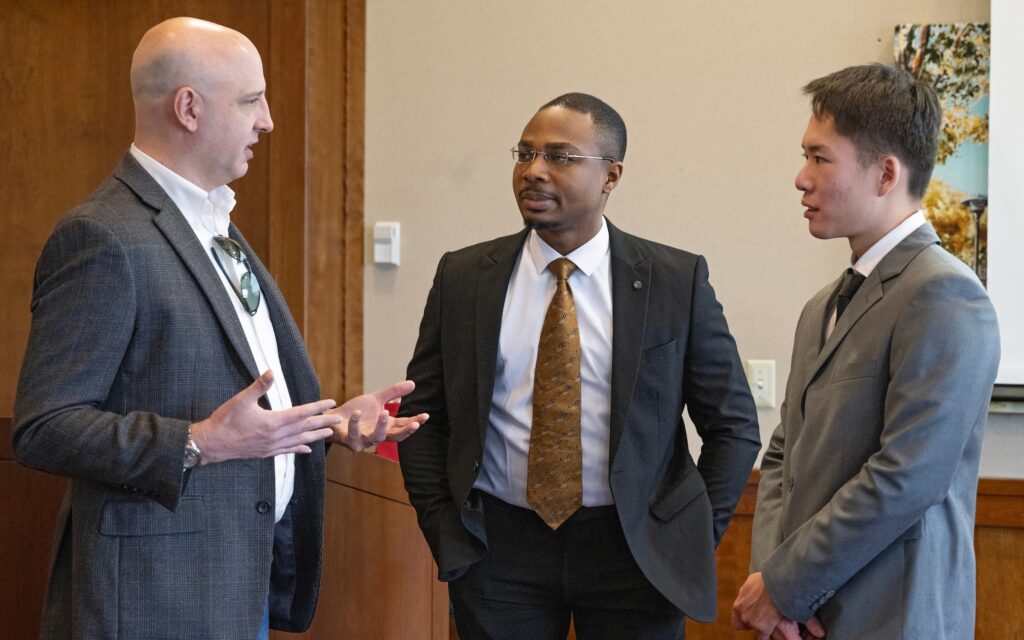 Three alumni stand in a circle and talk.