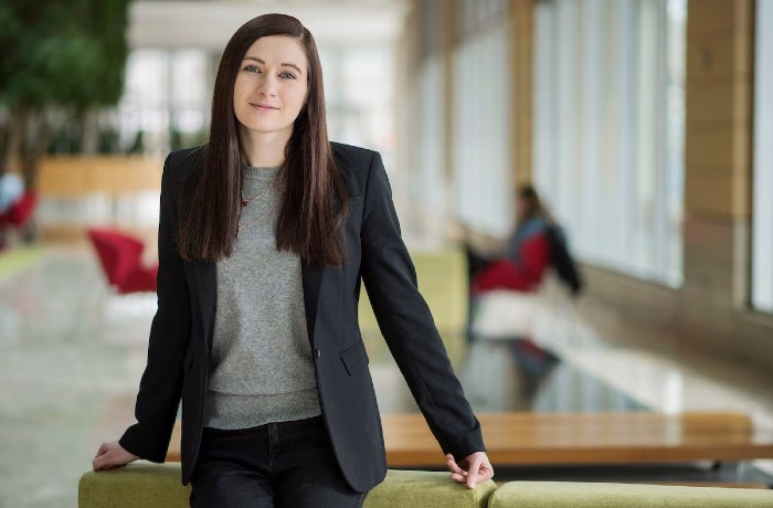 Jenna Herr in a black suit with gray shirt, standing in front of a large indoor space