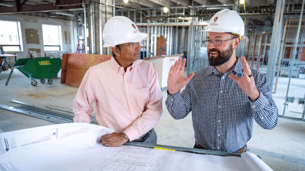 Dean Samba talks with a staff member while both wear hard hats.
