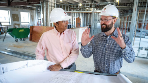 Dean Samba talks with a staff member while both wear hard hats.