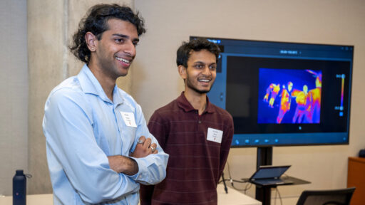 Two students stand near a display monitor and smile as they present their project at the Tech Exploration Lab open house.