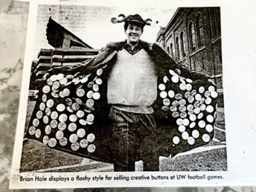 Brian Hale, as a student, holds out the sides of his coat, showing lots of buttons he is selling.