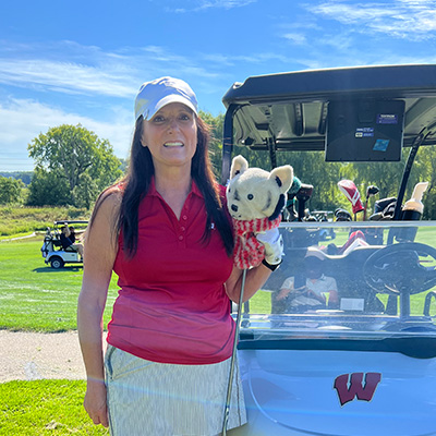 Brigitte Jagemann holds a golf club and poses in front of a golf cart with the UW athletics logo.