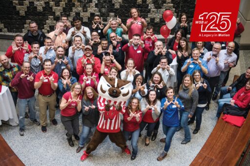 More than 50 individuals throw up the "W" sign during a group photo at the Homecoming Bash in Grainger Hall.