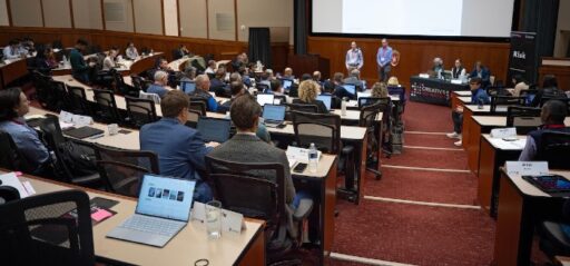 Two company founders standing in the front of CDL-Wisconsin's Large Room Discussion. Mentors, partners, and guests are seated in rows and moderators are seated in the front of the room.