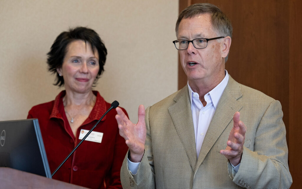 Nicholas Center director, Barb Bolens, looks on as Tom Tefft, Executive-in-Residence, speaks at a podium.