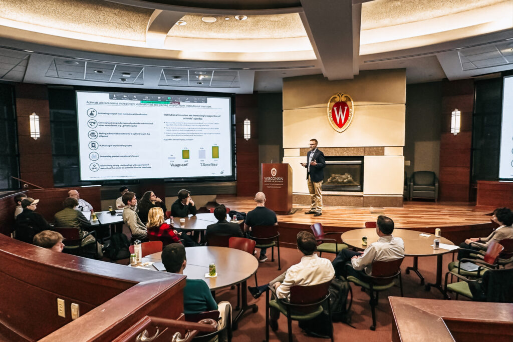 A speaker stands on stage and presents to a seated audience.