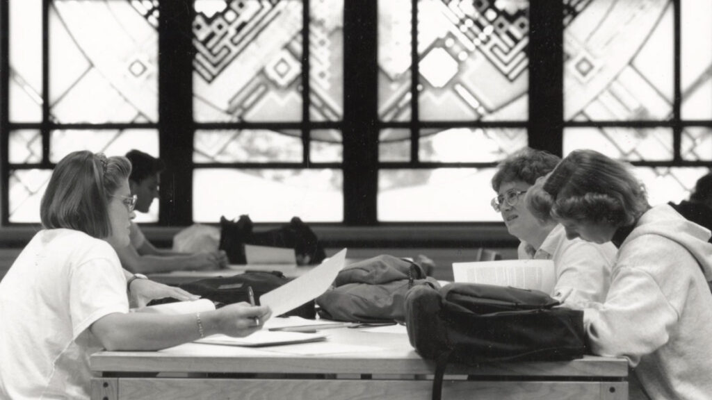 Students study in front of the Library Window art piece.