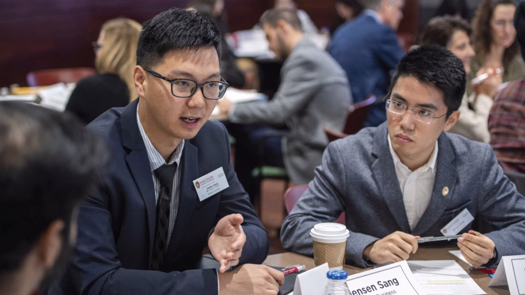 Two men sitting a table and talking with a group.