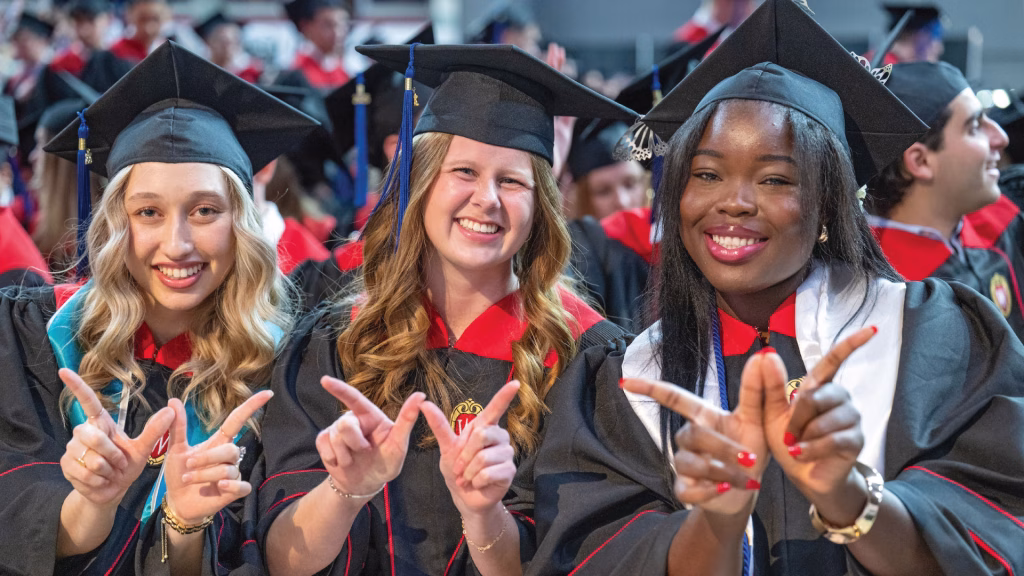 Three graduates from the Class of 2025 hold their hands in the shape of a W.