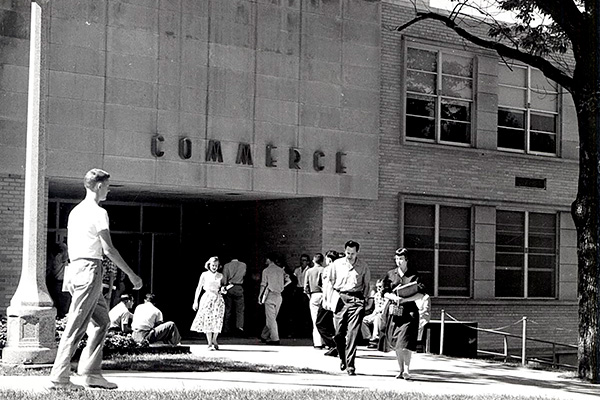 A black and white photo shows students walking to and from the Commerce building in 1955.