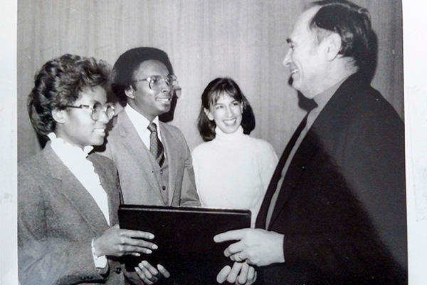 A black and white photo of a white man handing a black woman an official document while a black man and white woman stand nearby.