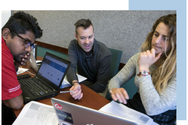 Three students sit at a table, in front of laptops, and discuss their task during WSB's first hackathon.