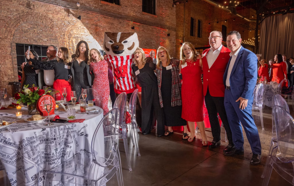 Under dim lights at WSB's anniversary gala, Bucky Badger and ten individuals link arms to sign and sway to the song Varsity.