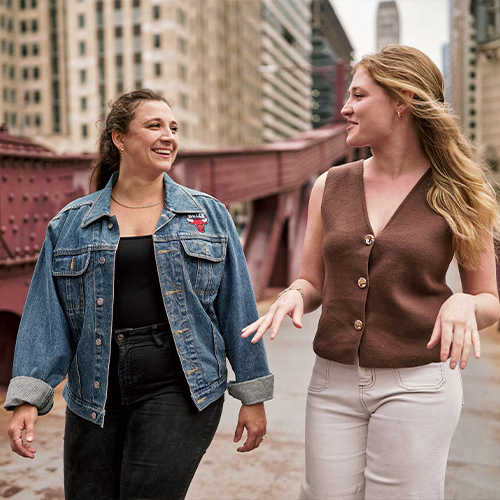 Abbe and her coworker smiling and talking as they walk on a bridge.