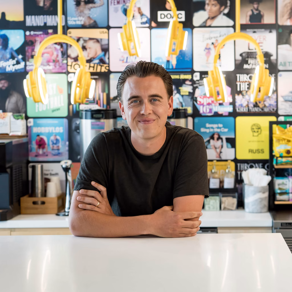 Anders smiling warmly at the camera in front of an art wall of music albums and headphones.