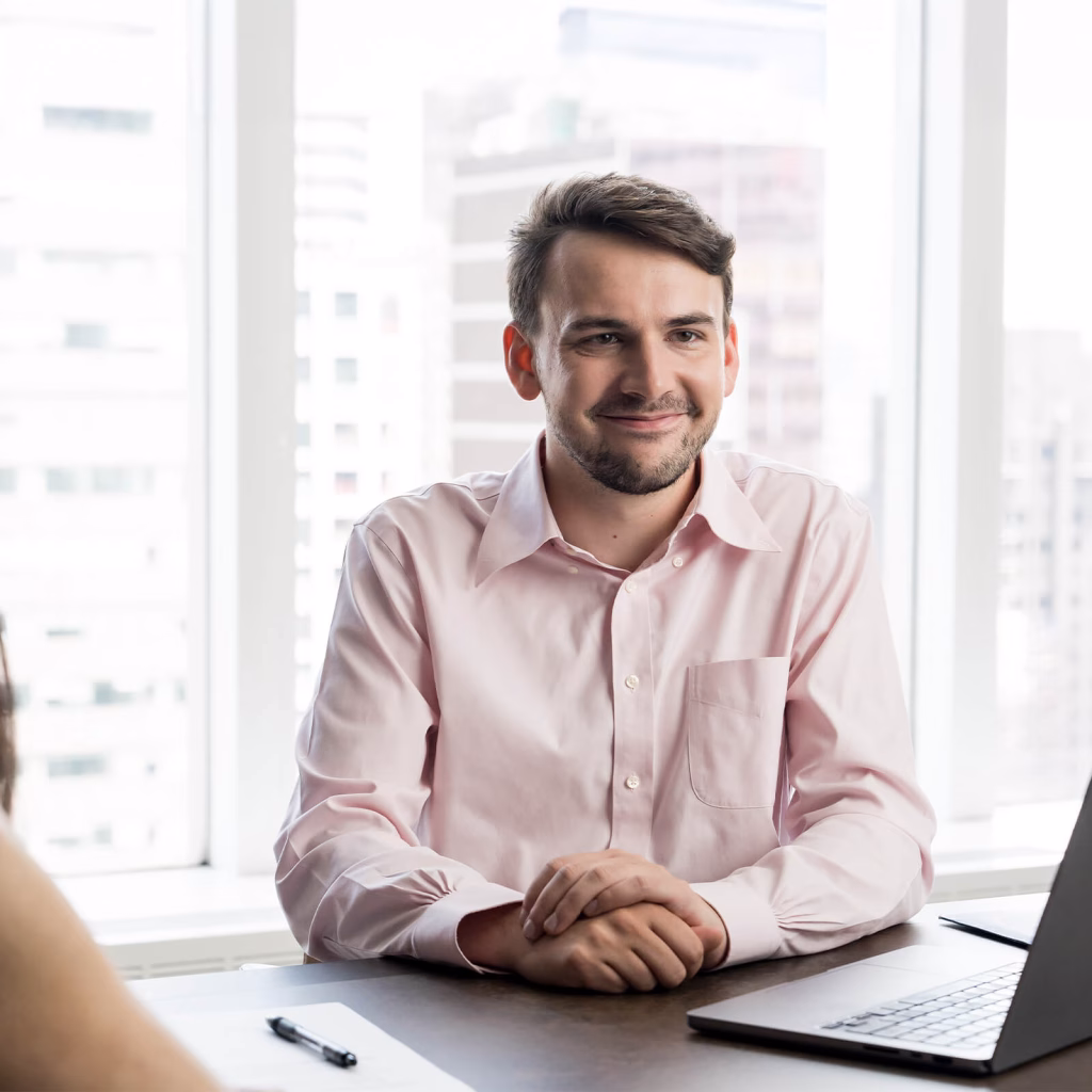 Charlie behind his laptop at a table, smiling at a coworker.