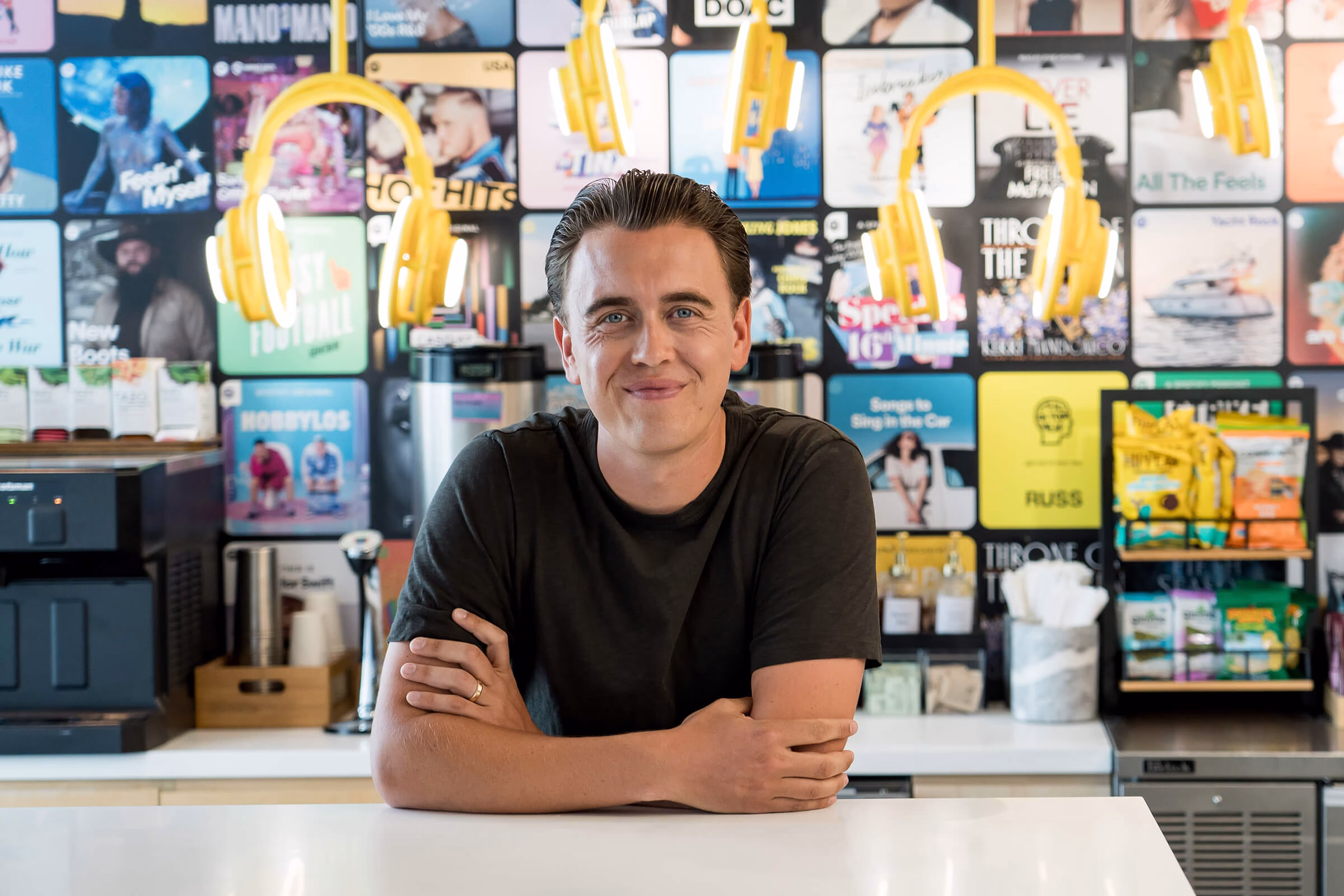 Anders smiling warmly at the camera in front of an art wall of music albums and headphones.