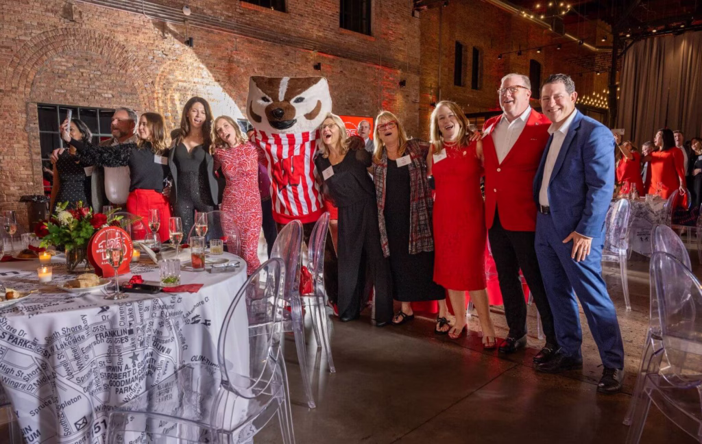 Well-dressed alumni and friends singing with their arms around each other and Bucky Badger.