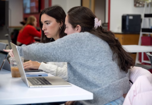 Two female students look at a laptop screen.