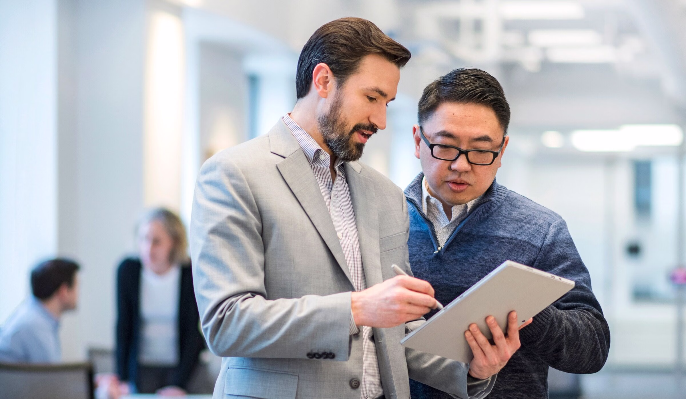 Two men talking while one holds a tablet and stylus.