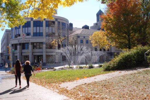 Two students are walking toward Grainger Hall in the autumn. Tree leaves have changed colors and some have falled to the ground.
