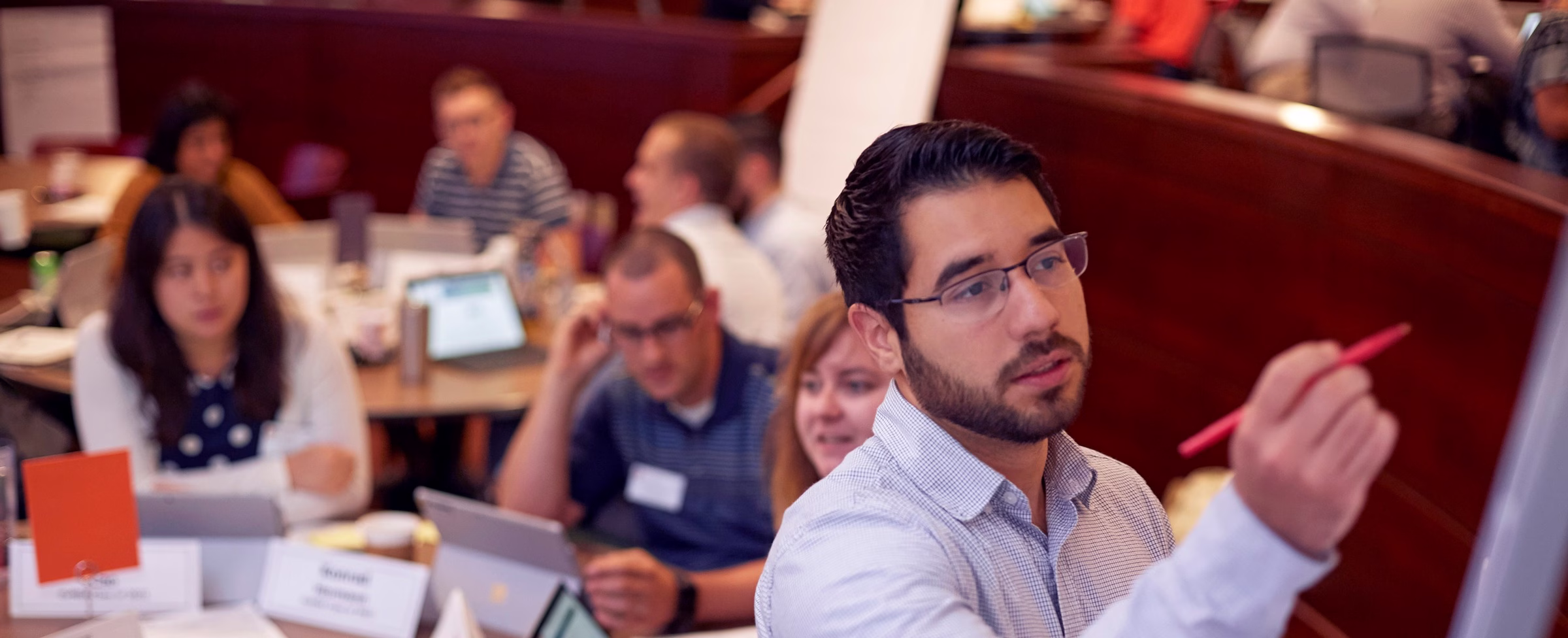 An MBA student writes on the board as classmates work on laptops.