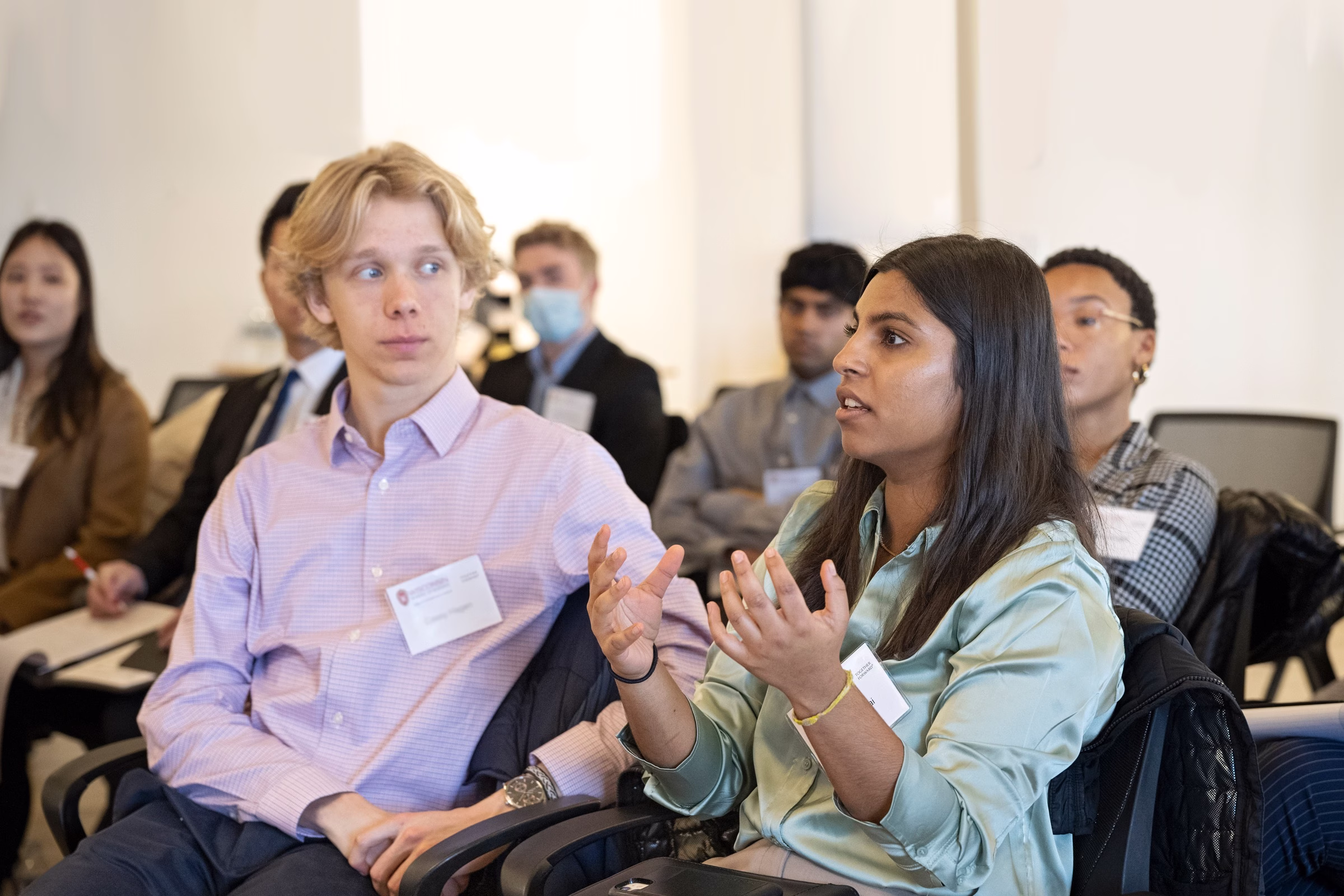 A student talks in class while the student sitting next to her watches and listens.