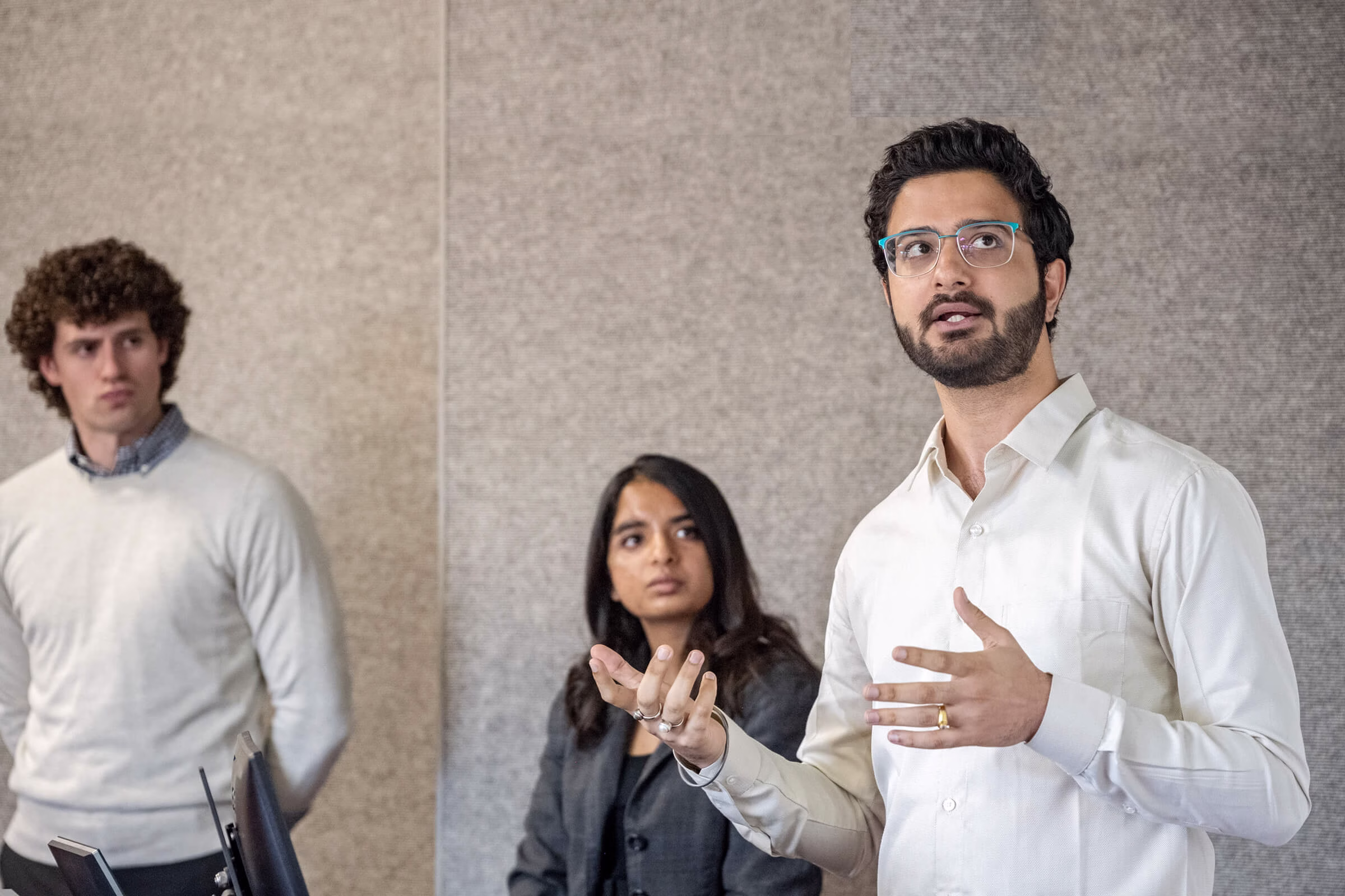 Two men and a woman standing in front of a monitor.