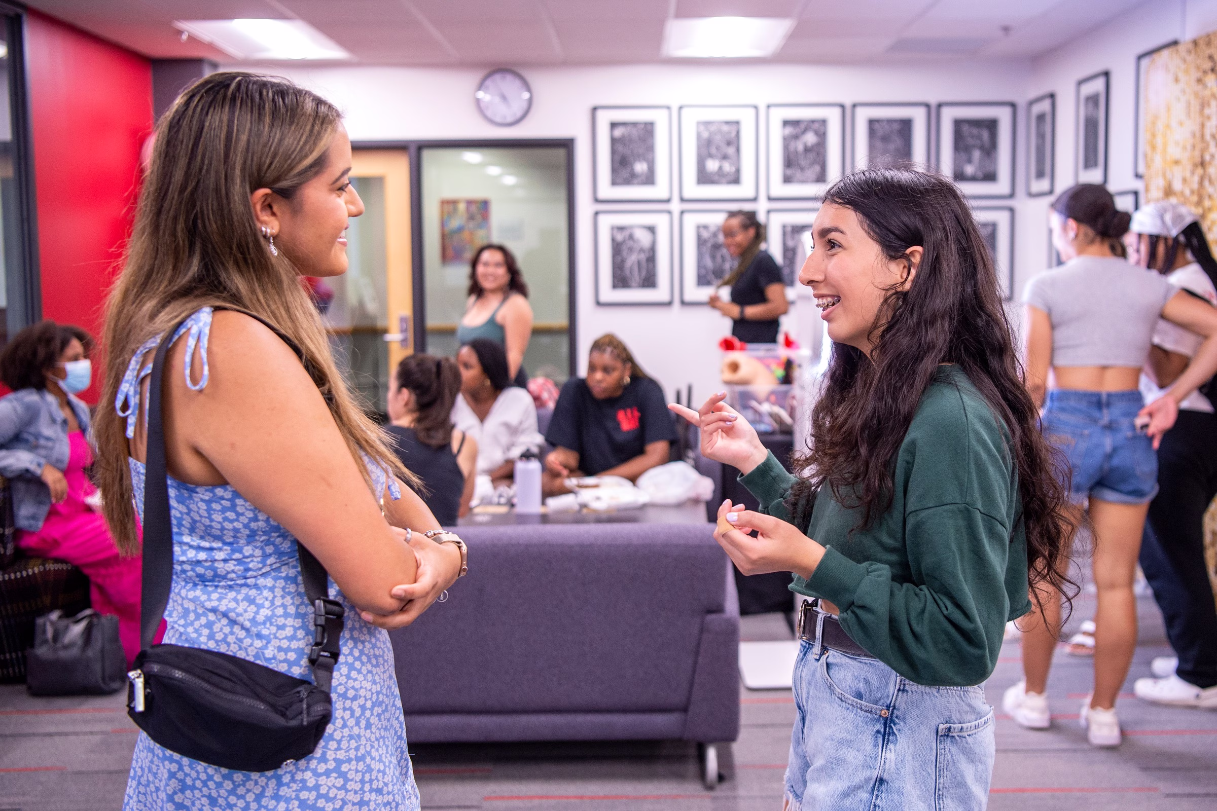 A racially diverse group of students are smiling and chatting in the Multicultural Center. Students can be seen sitting on couches in the background.