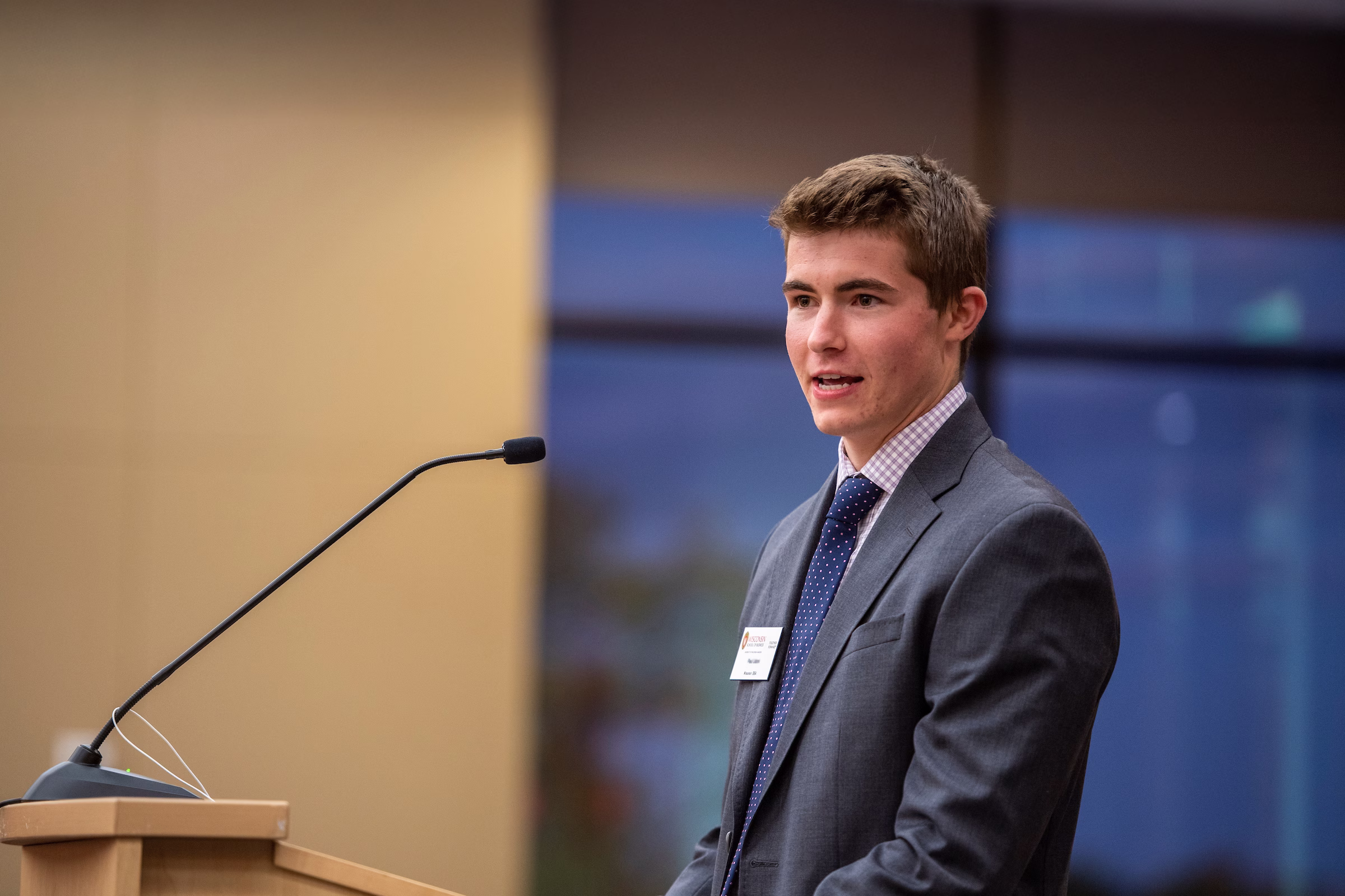 A male student stands in front of a microphone and speaks to a group.