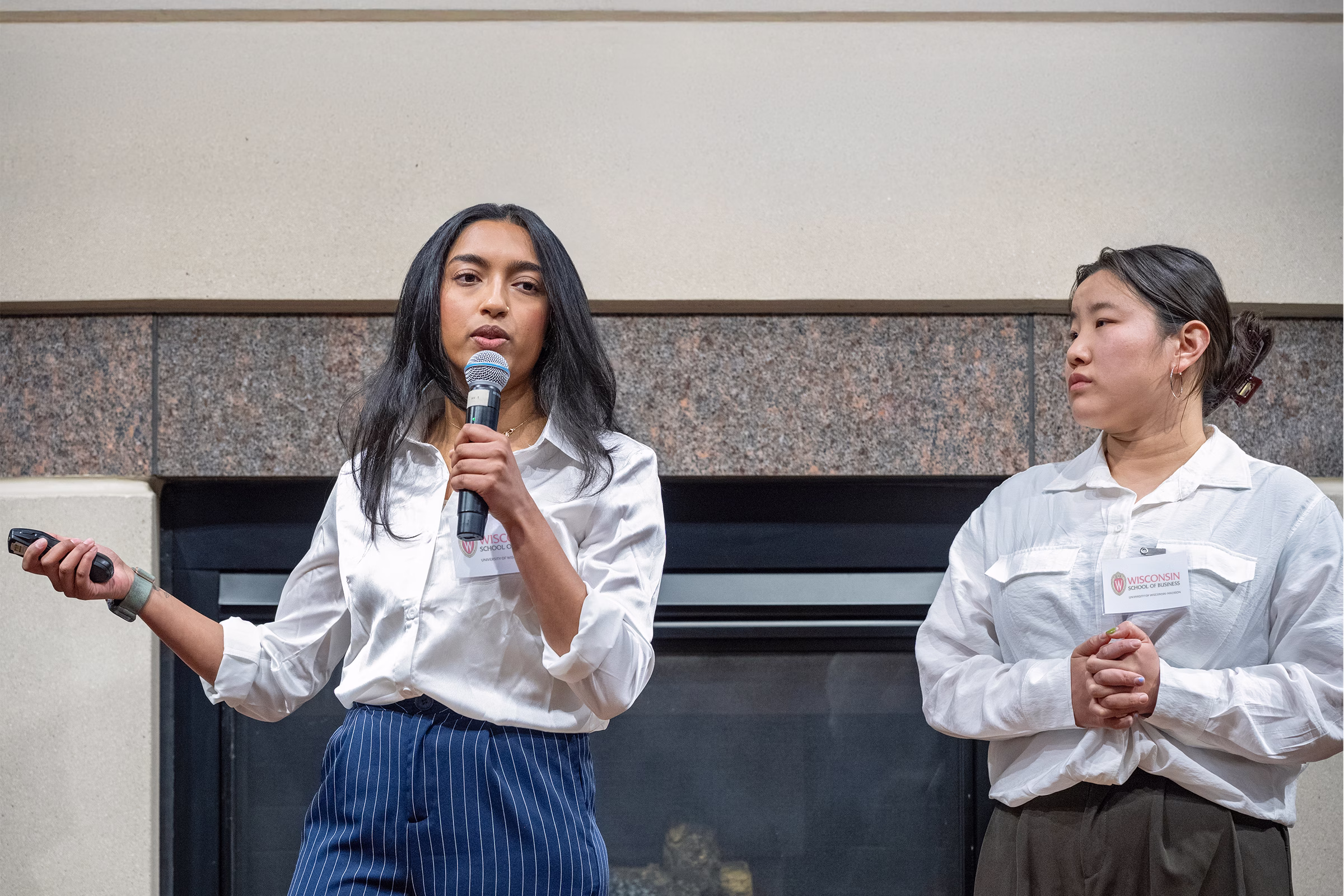 A female student wearing glasses and a pantsuit stands and presents in front of a slideshow.