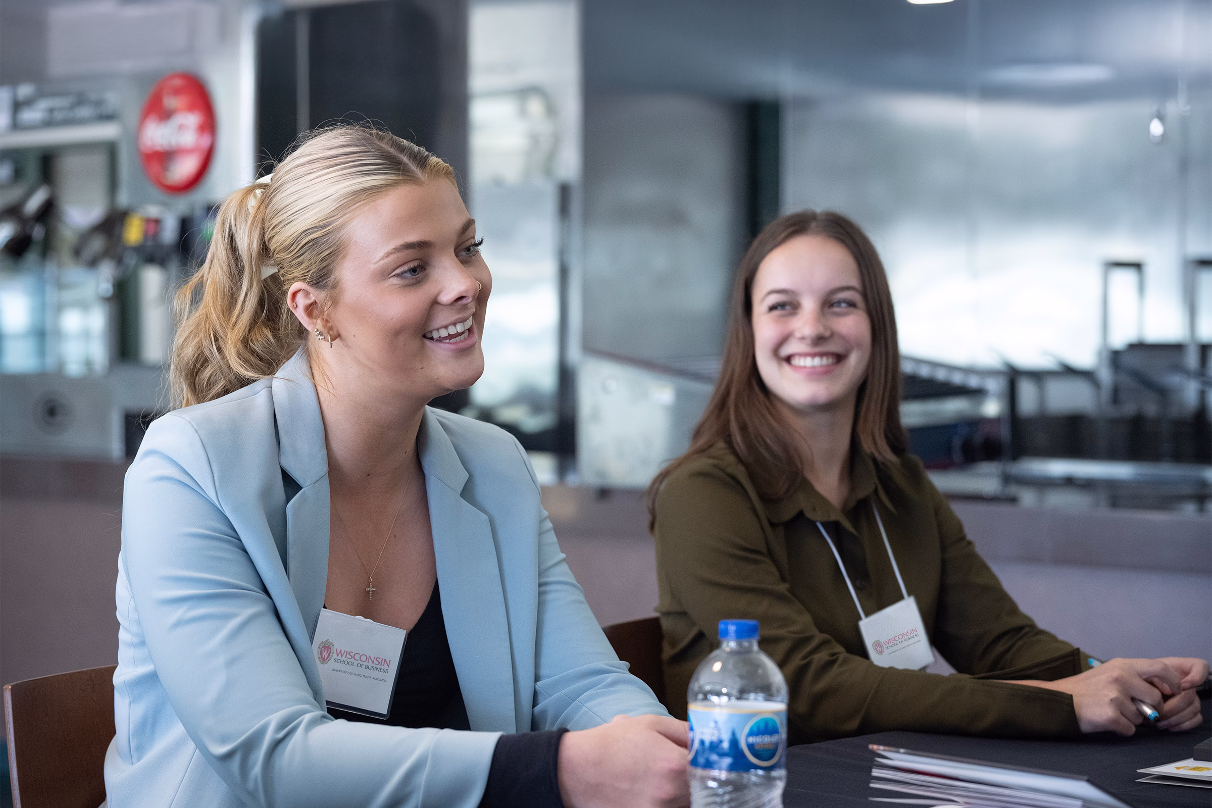 Two students smile while sitting next to each other at a table.