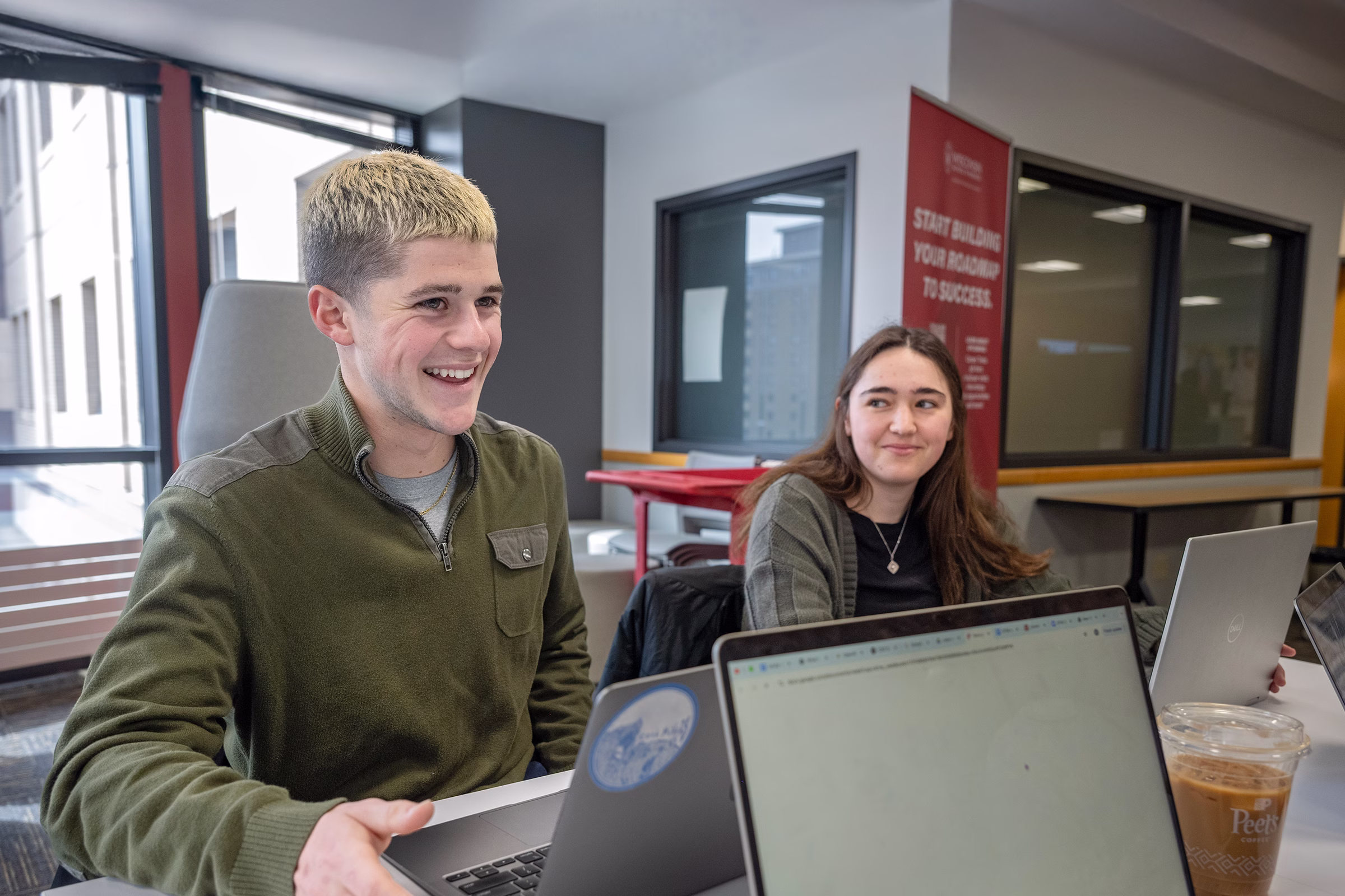 Two students smile while sitting next to each other at a table.