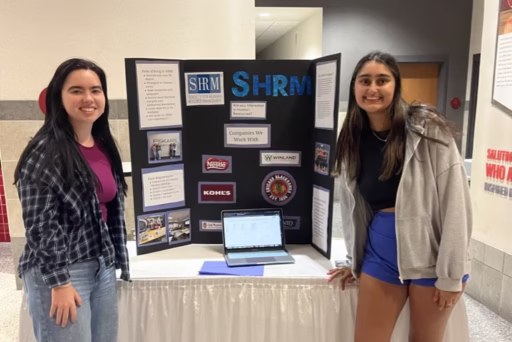 Two student representatives from the UW–Madison Society for Human Resource Management stand in front of a trifold board at a student org fair.