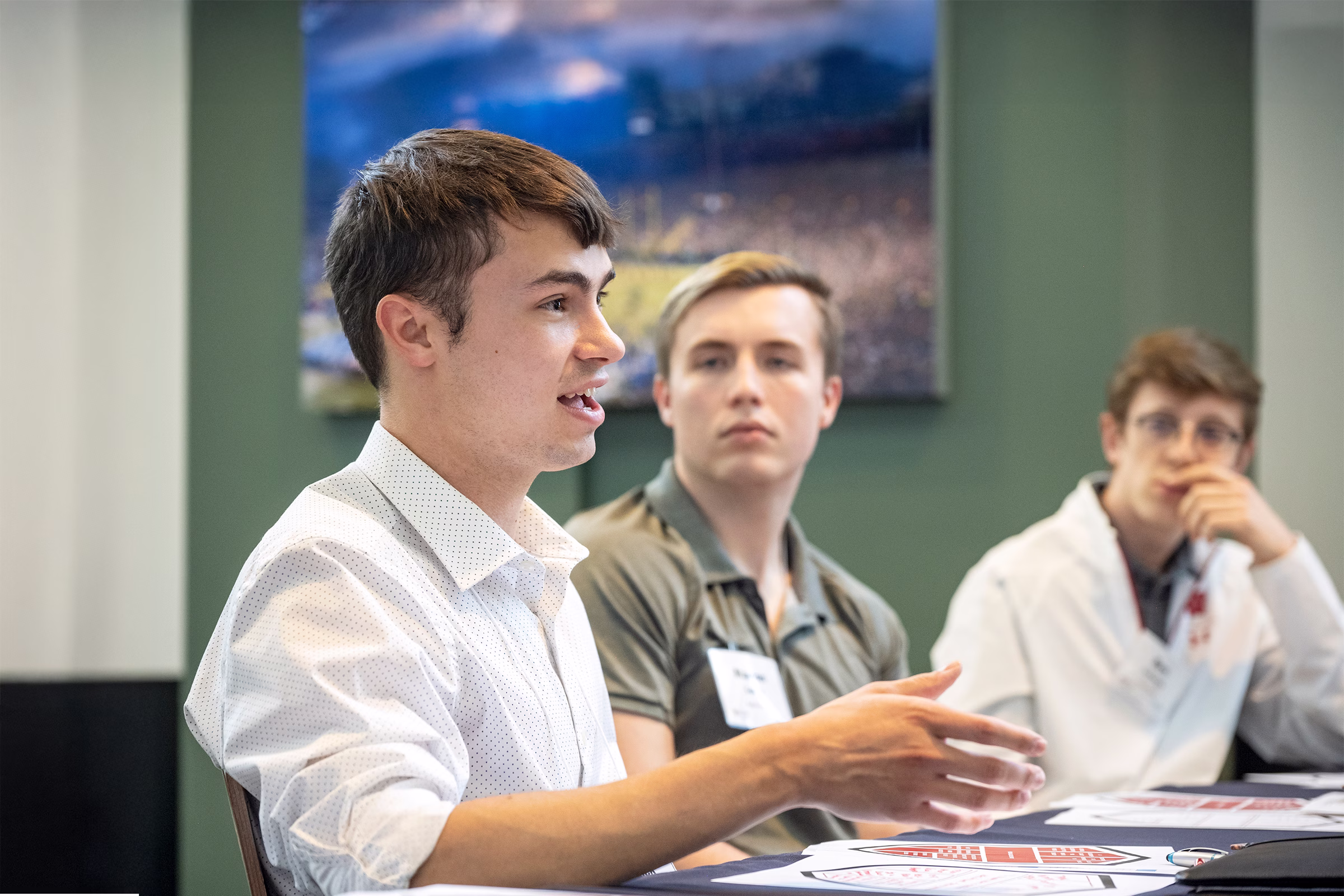 Three students sit at a table during class while one of them speaks.