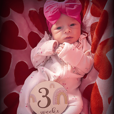 baby dressed in pink with sign that says: 3 weeks.