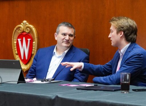 Justin Sydnor and Hayden Robinson are wearing suit jackets and seated at a table, talking.