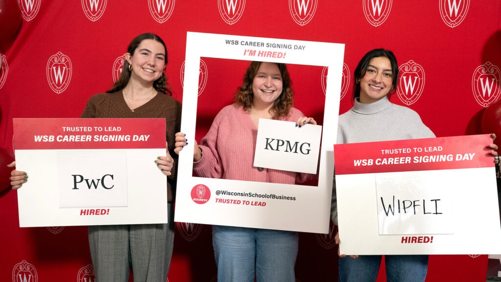 Three students proudly displaying the companies that hired them in WSB Career Signing Day.
