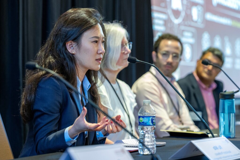 A woman speaks into a mic while seated next to fellow panelists.
