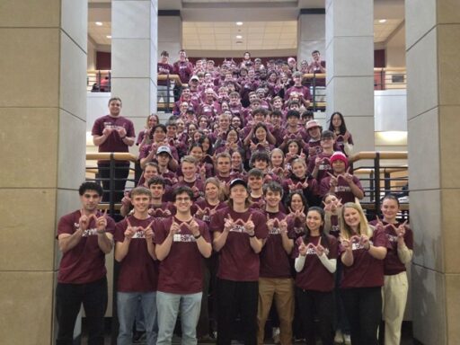 Large group of Actuarial Club students wearing matching club T-shirts pose together on the central staircase inside Grainger Hall.