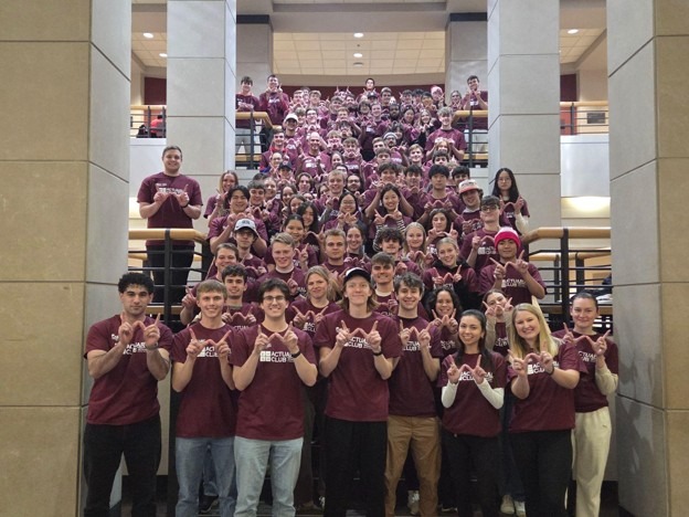 Large group of Actuarial Club students wearing matching club T-shirts pose together on the central staircase inside Grainger Hall.