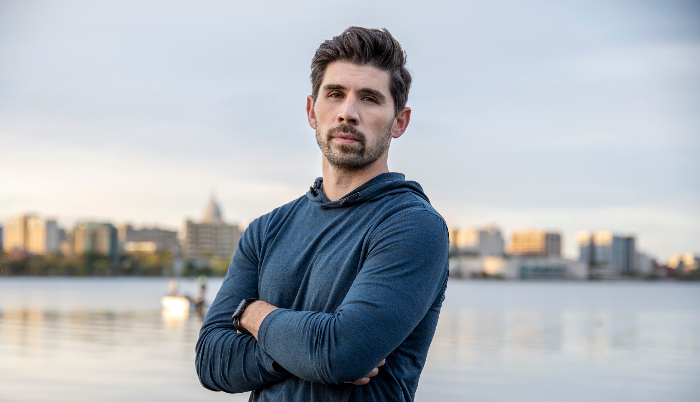 Kyle Nakatsuji stands in front of a lake and city skyline.