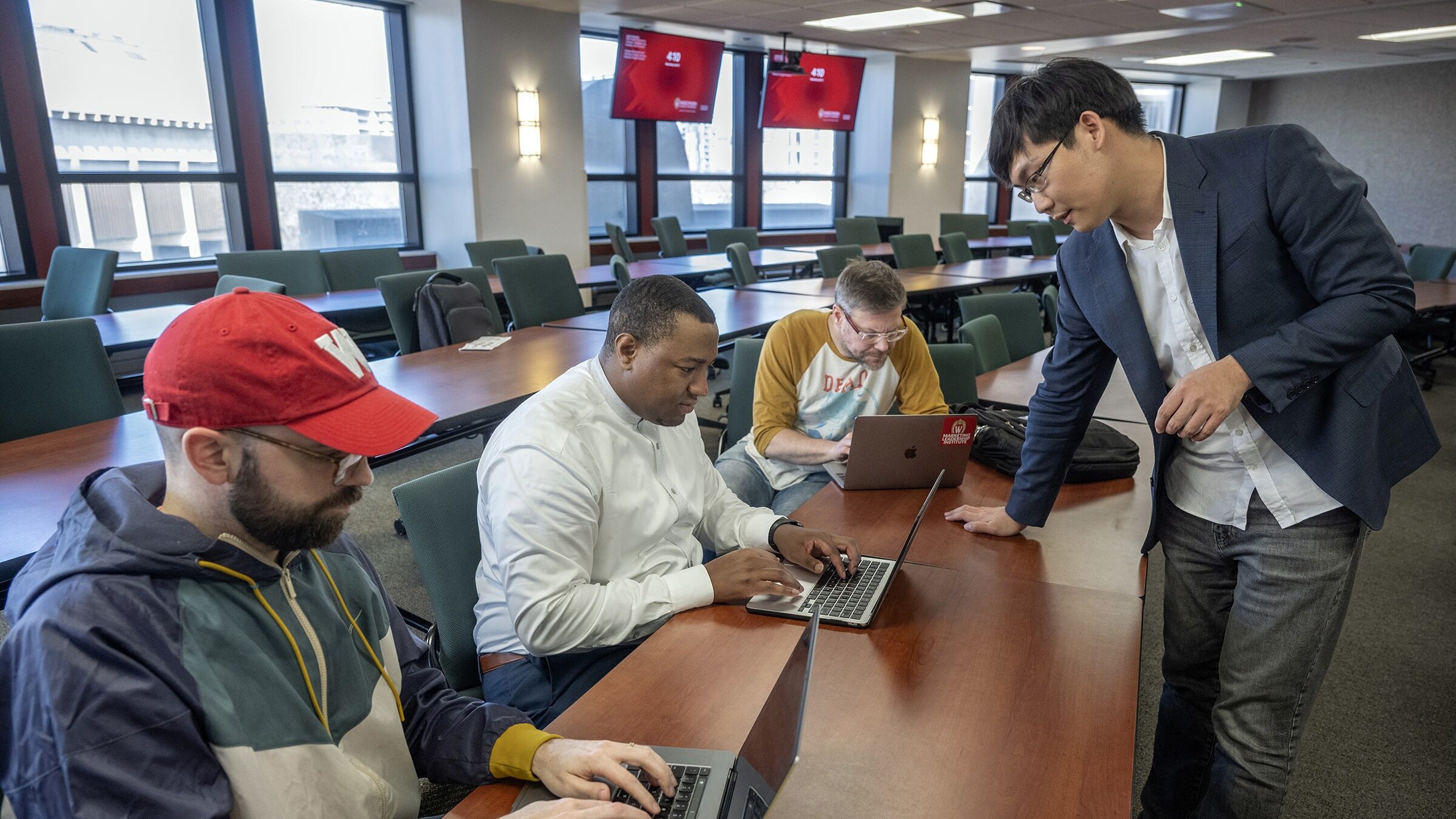 Professor Yi Liu talks with three students while they work on their laptops.