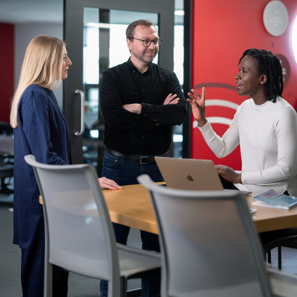 Three people standing around a table and talking.